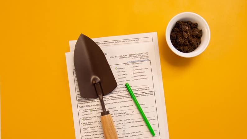 soil test form with pen, trowel, and soil sample on a gold background